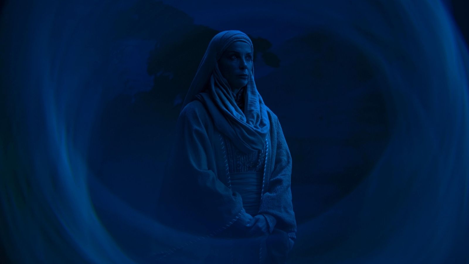 Mavi ışık efektleriyle gece atmosferinde kostümlü bir karakter, çöl arka planı.